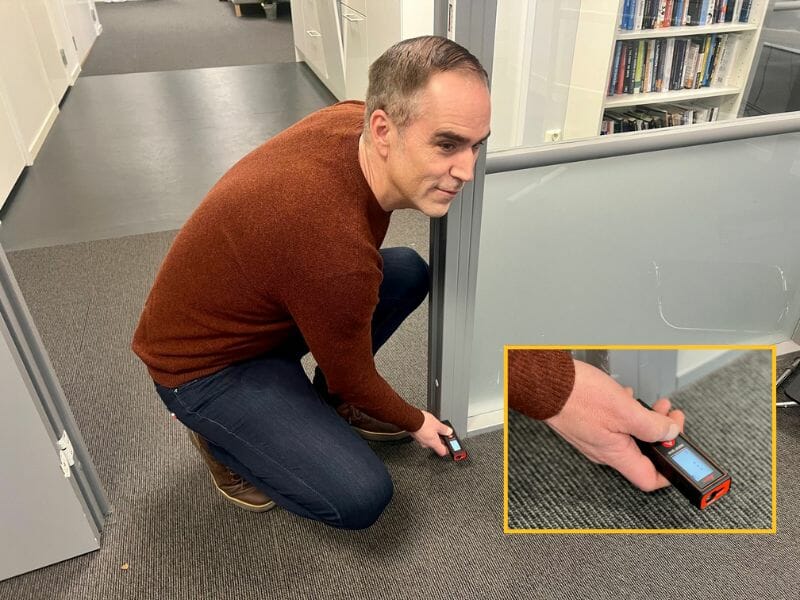 Man using a laser measure to determine square footage of a room.